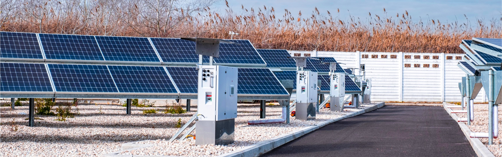 Impianto fotovoltaico con pannelli solari disposti su terreno ghiaioso, affiancati da centraline elettriche