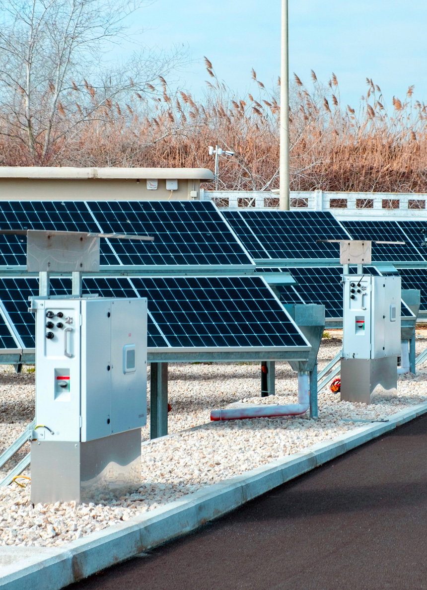 Impianto fotovoltaico con pannelli solari disposti su terreno ghiaioso, affiancati da centraline elettriche