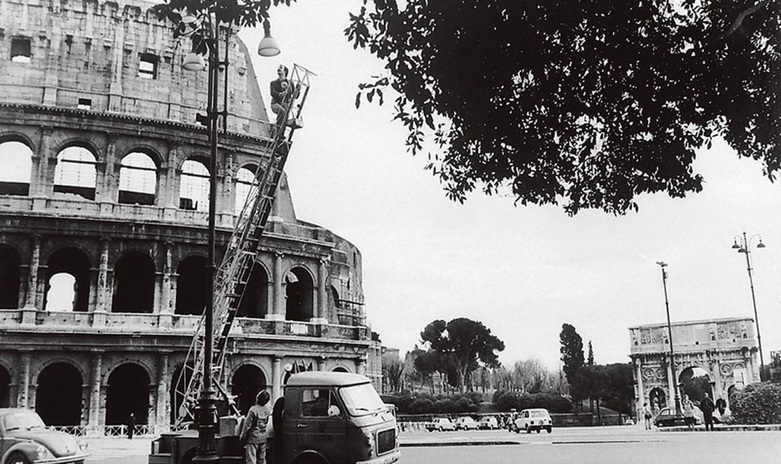 Fotografia d'epoca di un camion ACEA con operai che lavorano all'illuminazione vicino al Colosseo, simbolo dei piani di sviluppo della città