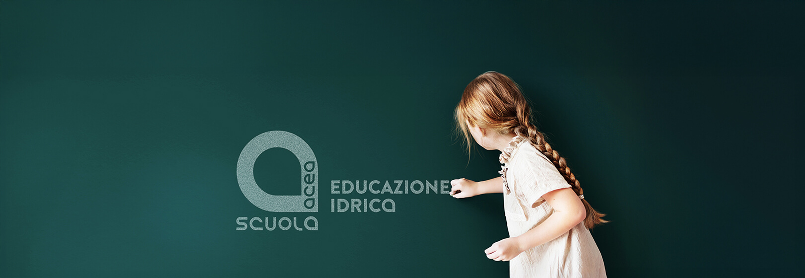 A little girl draws the logo of her school with chalk on the blackboard