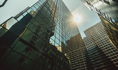 Vista dal basso di grattacieli con finestre riflettenti e il sole che splende nel cielo