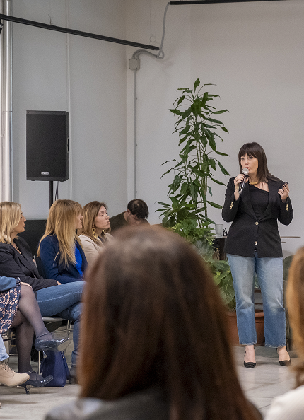 Una classe di persone assiste ad una lezione. Si intravede una slide proiettata e c'è un docente che parla tenendo in mano uno strumento di lavoro, oggetto della lezione