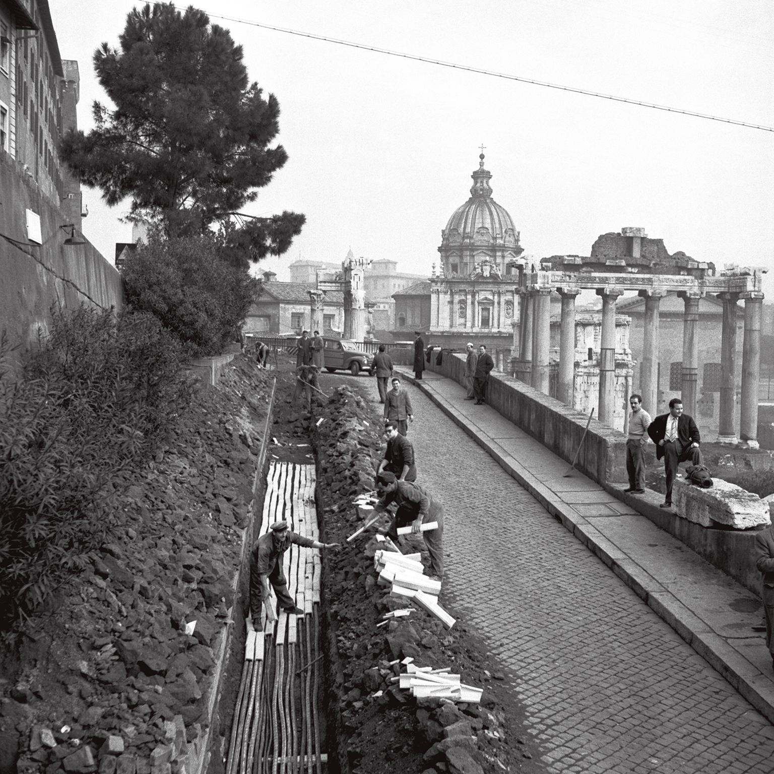 Foto in bianco e nero di operai che scavano per creare le tubature dell'acquedotto, con il Vaticano sullo sfondo