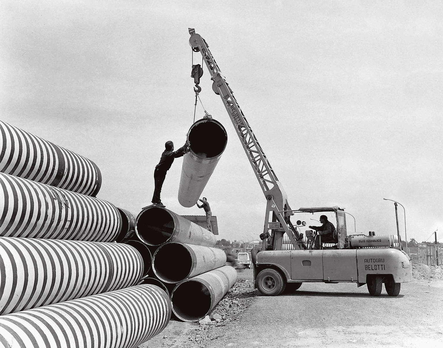 foto in bianco e nero di una vecchia gru che solleva dei grossi tubi
