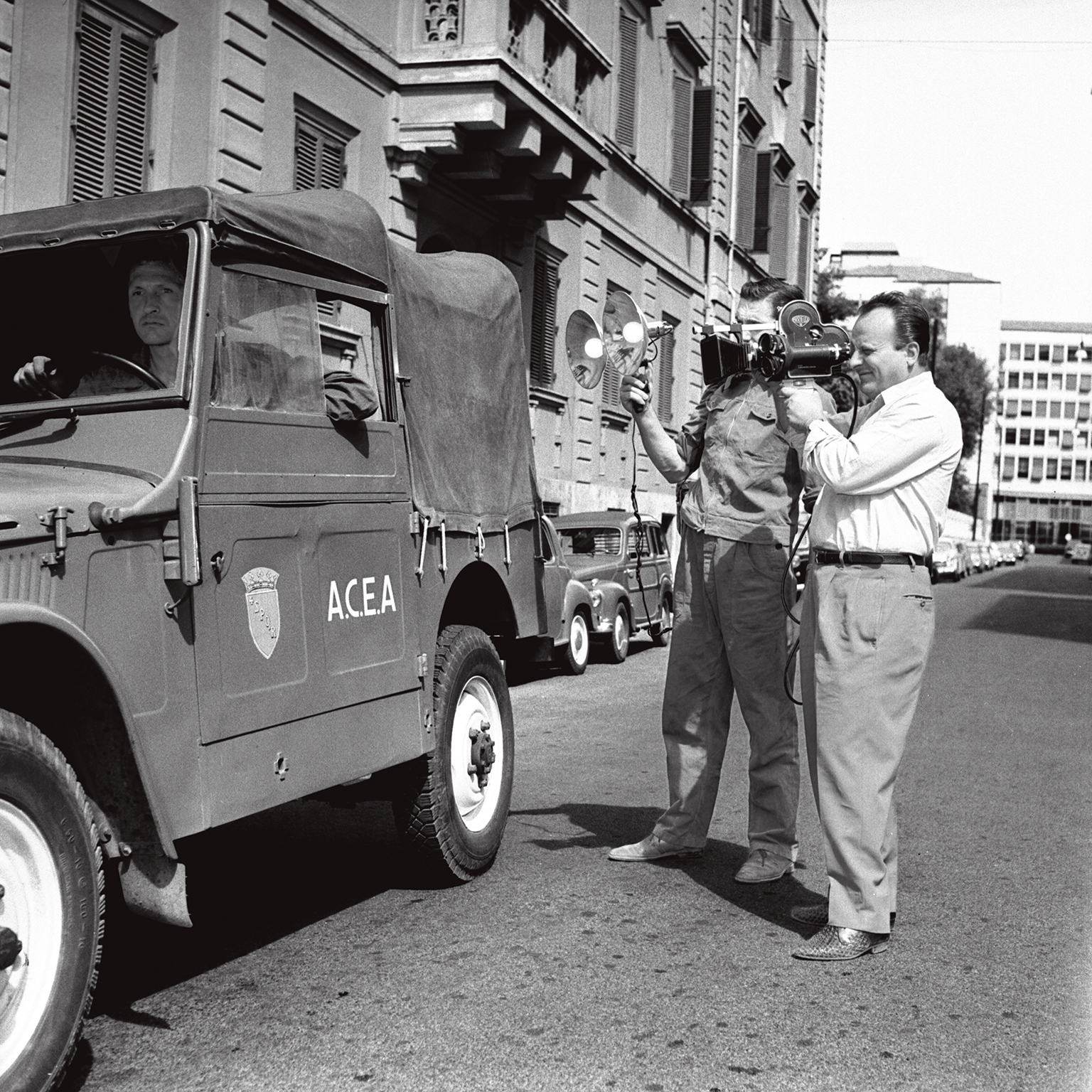 foto in bianco e nero di reporter che registra con la cinepresa un antico furgone con logo acea