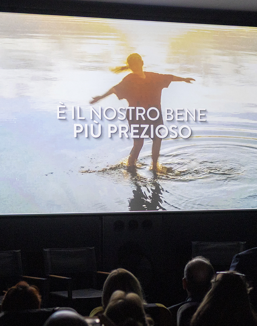 Immagine di una donna con le braccia aperte, con i piedi immersi nell'acqua, e il testo "è il nostro bene più prezioso" proiettata sul grande schermo durante la conferenza stampa Acea "Festa del Cinema"