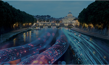 Sullo sfondo il Vaticano e davanti un ponte, entrambi illuminati. Sovrapposto sul Tevere passano dei cavi elettrici colorati