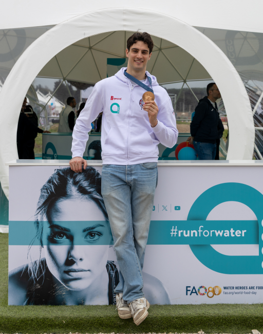 Giovane atleta sorridente mostra la medaglia della ACEA Run Rome the Marathon 2024 davanti al pannello con hashtag runforwater