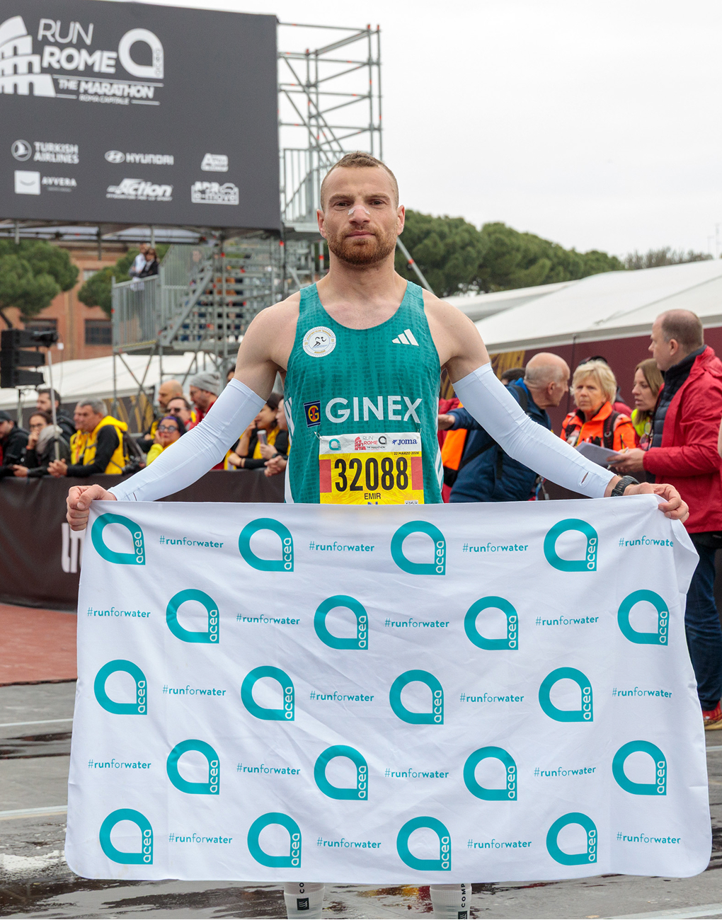 An athlete smiles as he holds up a towel featuring the Acea logo