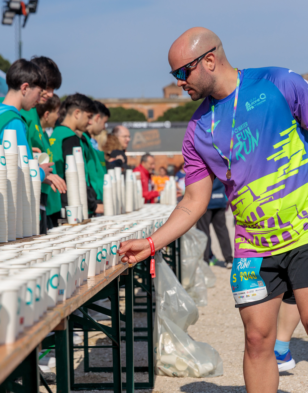 An athlete picks up a glass of water bearing the Acea logo from a refreshment station at the Acea Run Rome Marathon