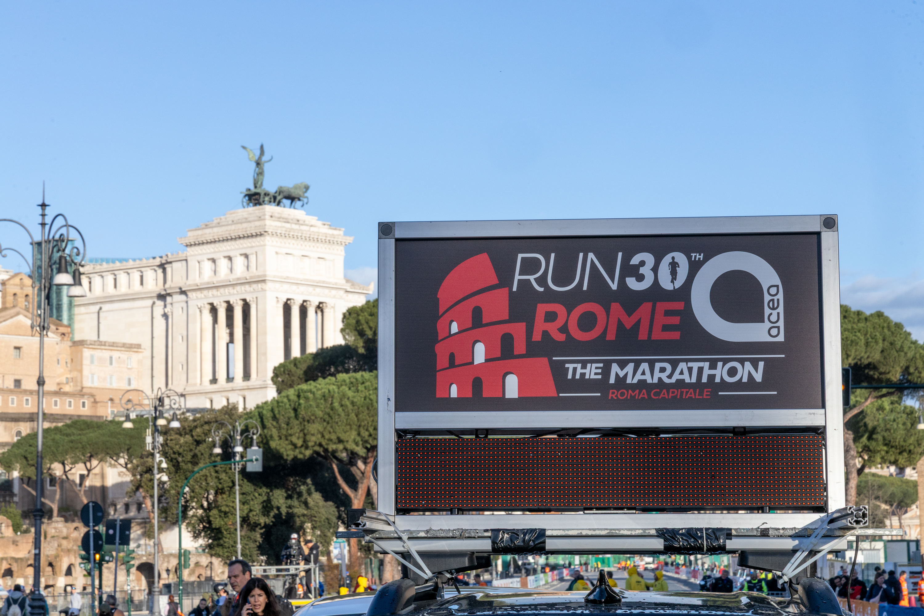 Cartellone dell'evento con scritto "run rome 30 the marathon" e il logo acea. Alle spalle del cartellone si vede l'altare della Patria