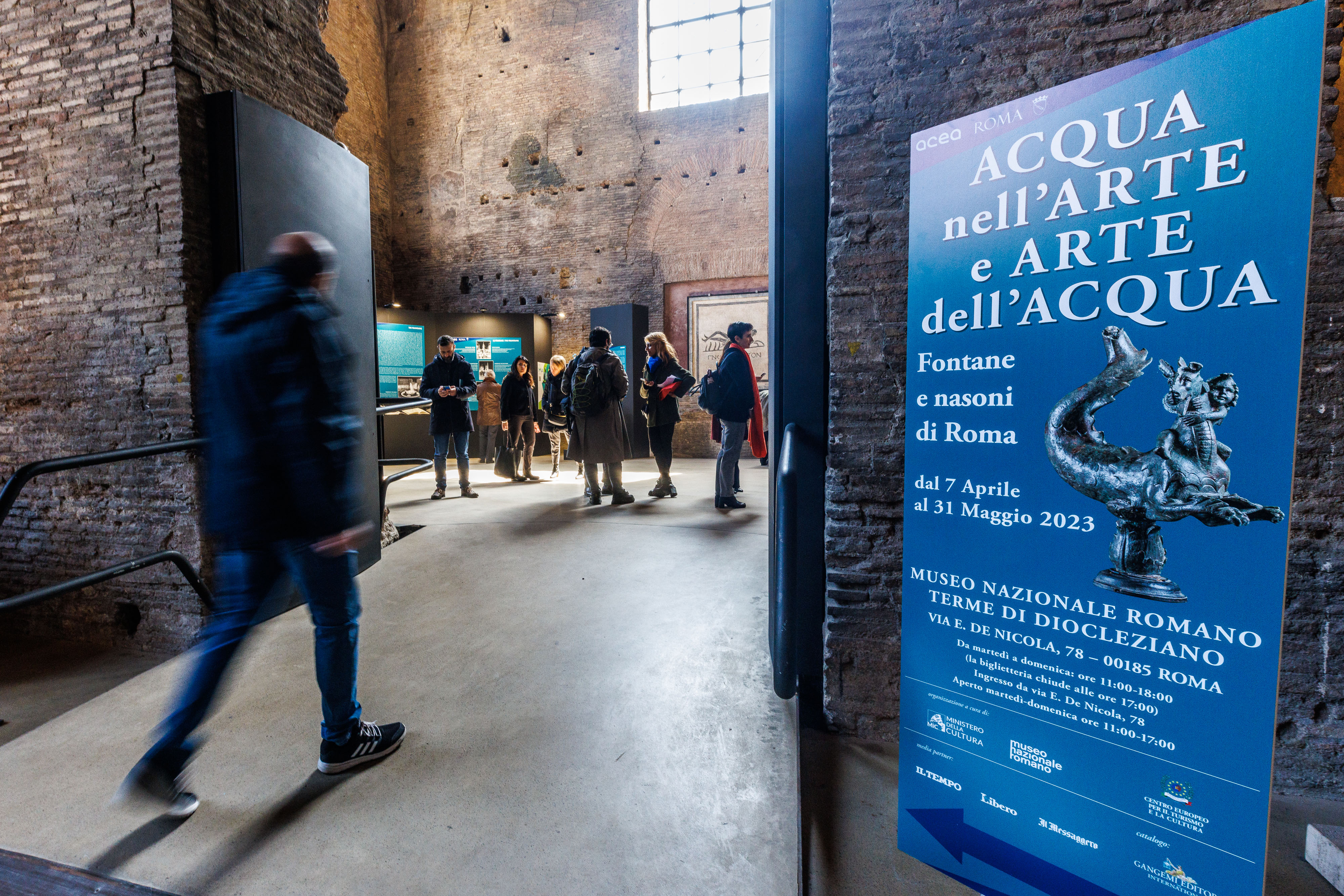 alcune persone che assistono alla mostra, inoltre si vede un poster con la locandina dell'evento