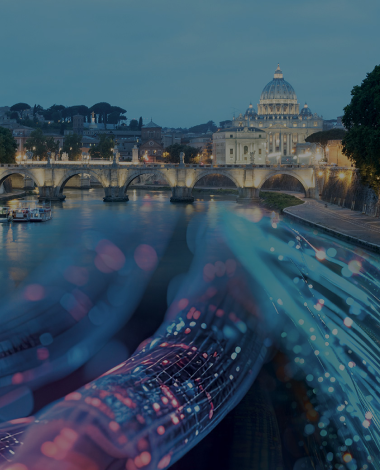 Sullo sfondo c'è il Vaticano e davanti un ponte, entrambi illuminati. Sovrapposto sul Tevere passano dei cavi elettrici colorati