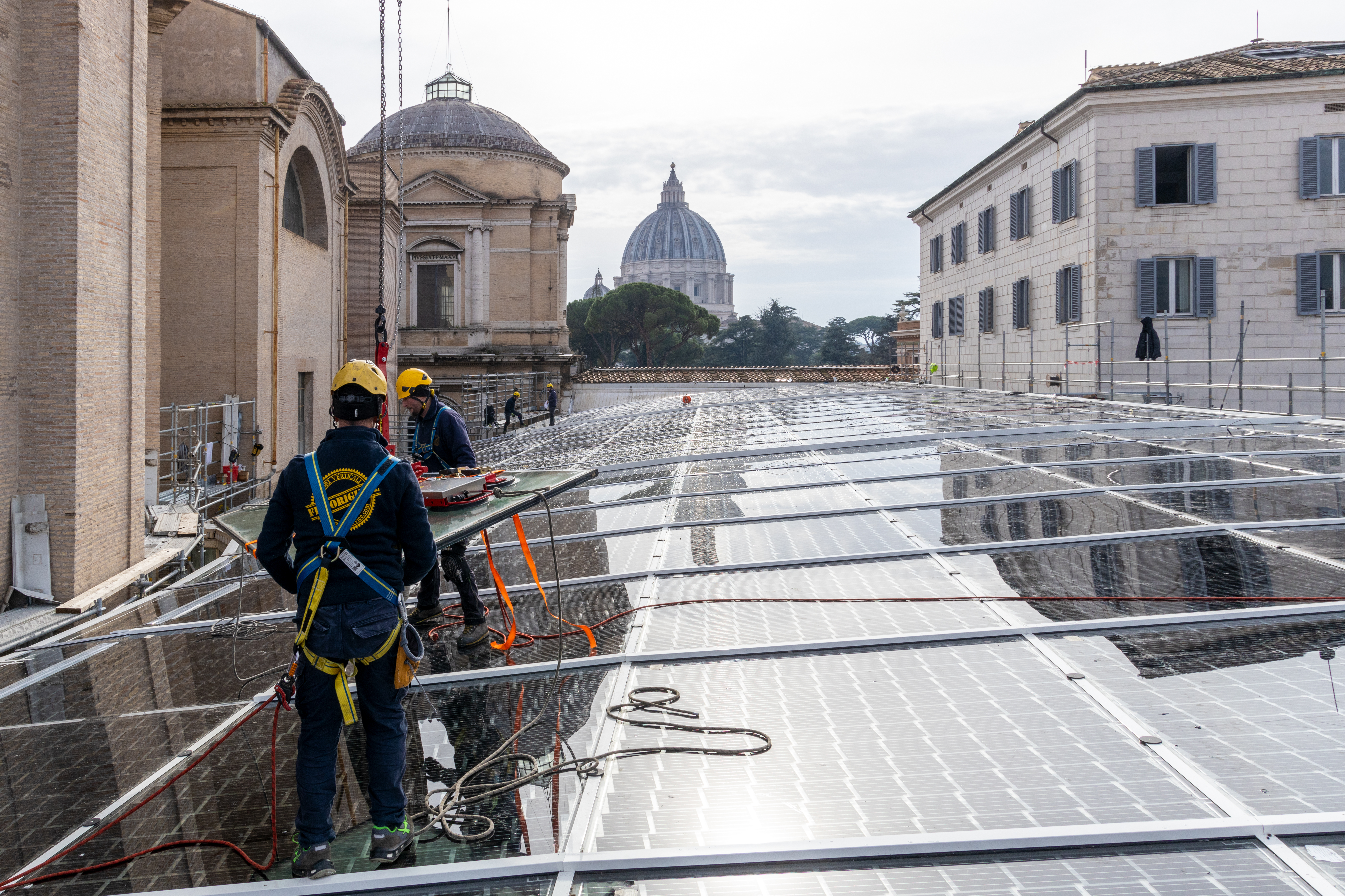 two workers installing photovoltaic panels with st. peter's basilica visible in the distance