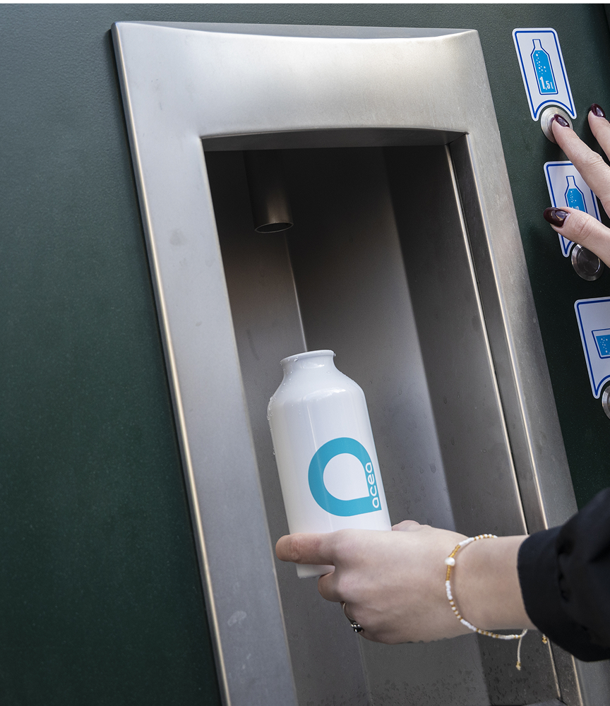 una persona che riempie un aborraccia con il logo di Acea ad una casa dell'acqua