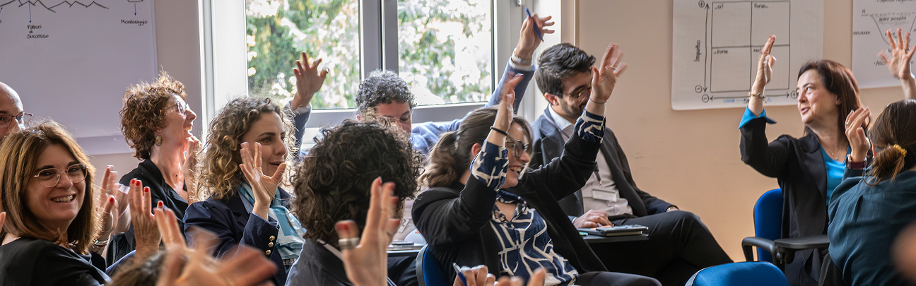 Un gruppo diversificato di professionisti partecipa attivamente a una sessione collaborativa, alzando le mani in segno di partecipazione. L'ambiente luminoso e l'entusiasmo dei partecipanti riflettono i valori di inclusione, diversità e collaborazione promossi da Acea.