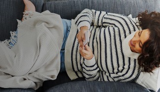 Foto di donna stesa sul divano che utilizza lo smartphone.