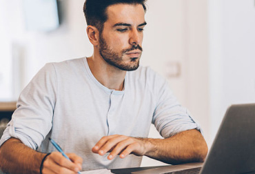 Ragazzo che scrive su un foglio davanti al computer