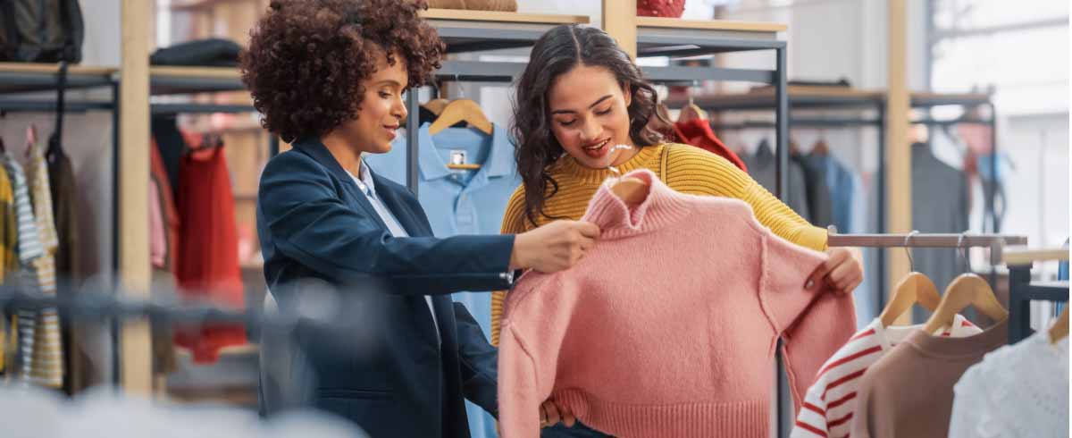 All'interno di un negozio di abbigliamento, una commessa sta mostrando ad una cliente un maglione