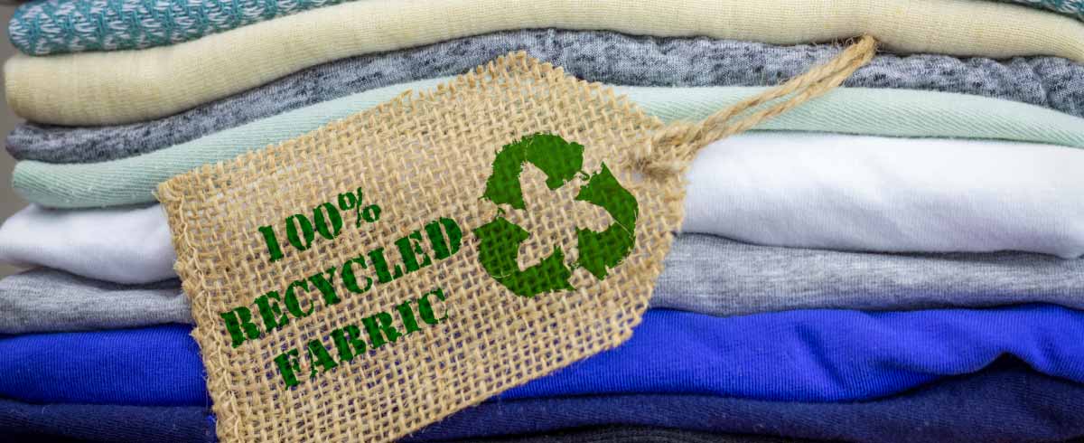 Pila di capi di abbigliamento con etichetta sulla sostenibilità "100% tessuti riciclati"