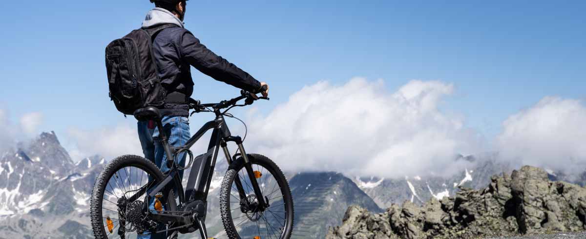 Foto di un ciclista in alta quota; è in piedi accanto alla sua Mountain Bike e fermo osserva il panorama roccioso che lo circonda.