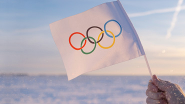 Una mano regge una bandiera bianca, dove sono raffigurati i 5 cerchi olimpici.
